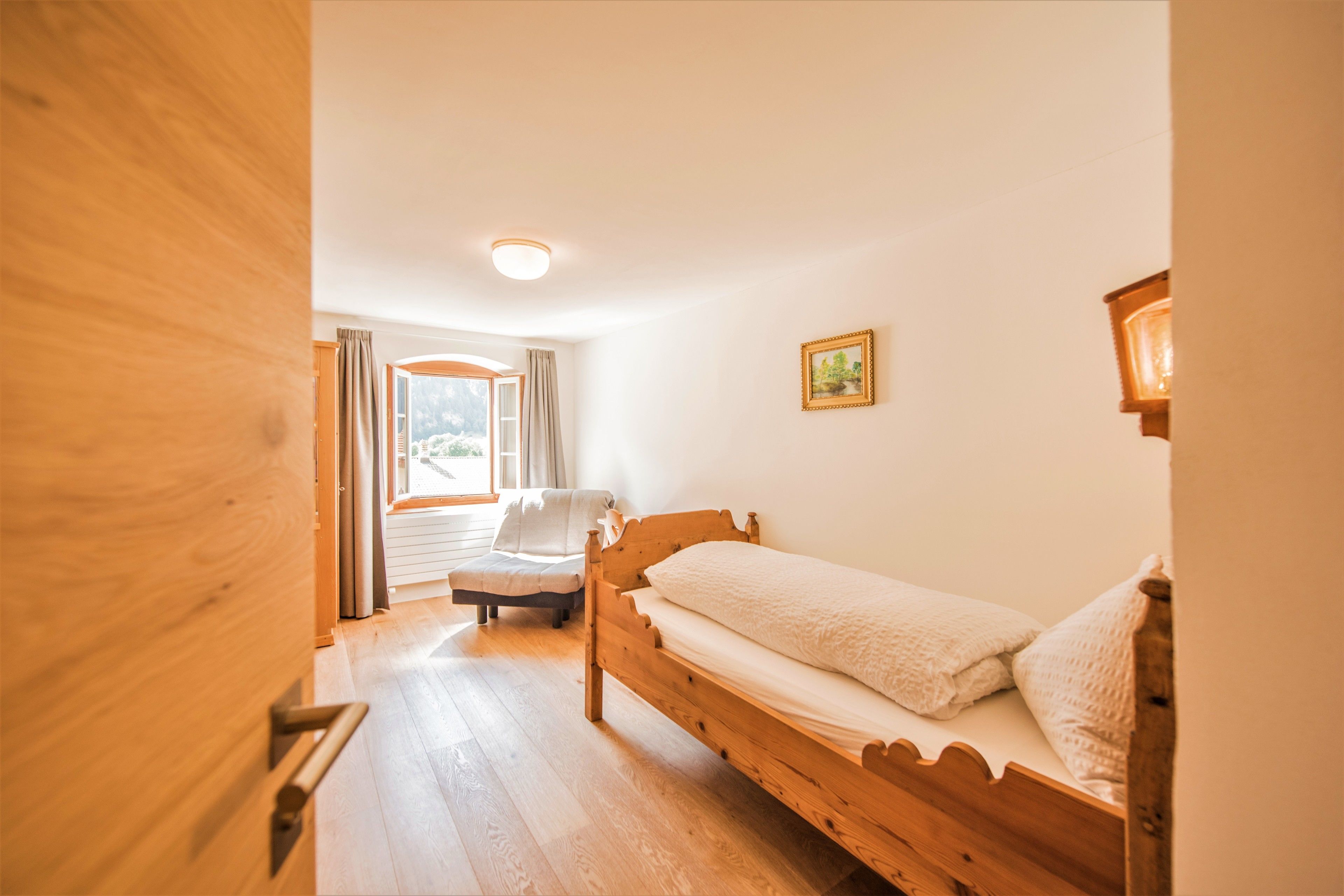 Un letto di legno in una stanza con una finestra, una sedia e un quadro appeso al muro.