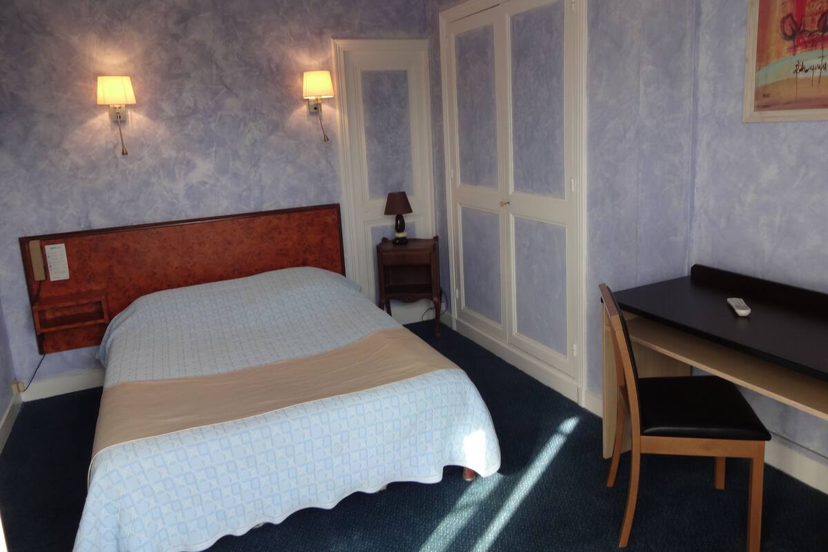 Een hotelkamer met een bed, een bureau, een stoel, een nachtkastje en twee wandlampen.