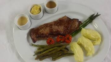 Ein Teller mit einem Steak, Spargel, Cocktailtomaten, Kartoffelpüree und drei kleinen Soßen.
