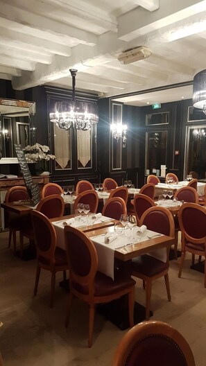Uma sala de jantar com várias mesas preparadas para os hóspedes, cada uma com cadeiras e louças.