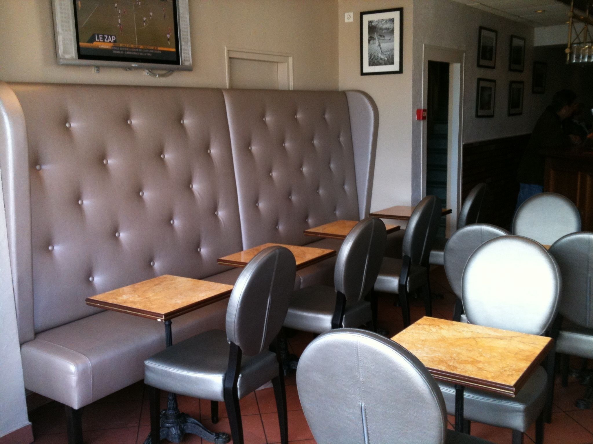 Ein Restaurantinneres mit einer gepolsterten Sitzecke, einzelnen Tischen mit Stühlen und einem an der Wand befestigten Fernseher.