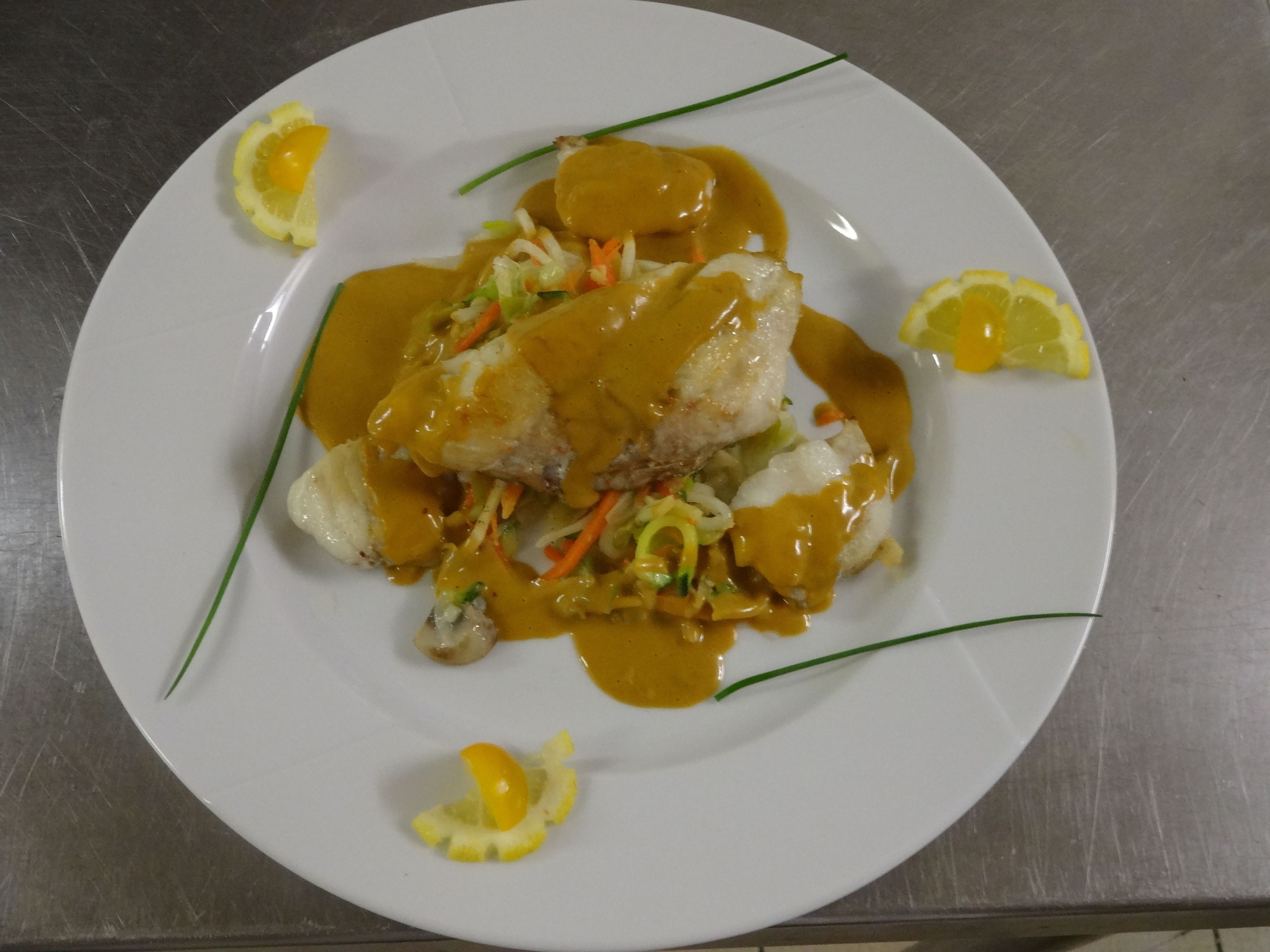 Um prato branco com um prato de peixe, decorado com fatias de limão e cebolinha verde.