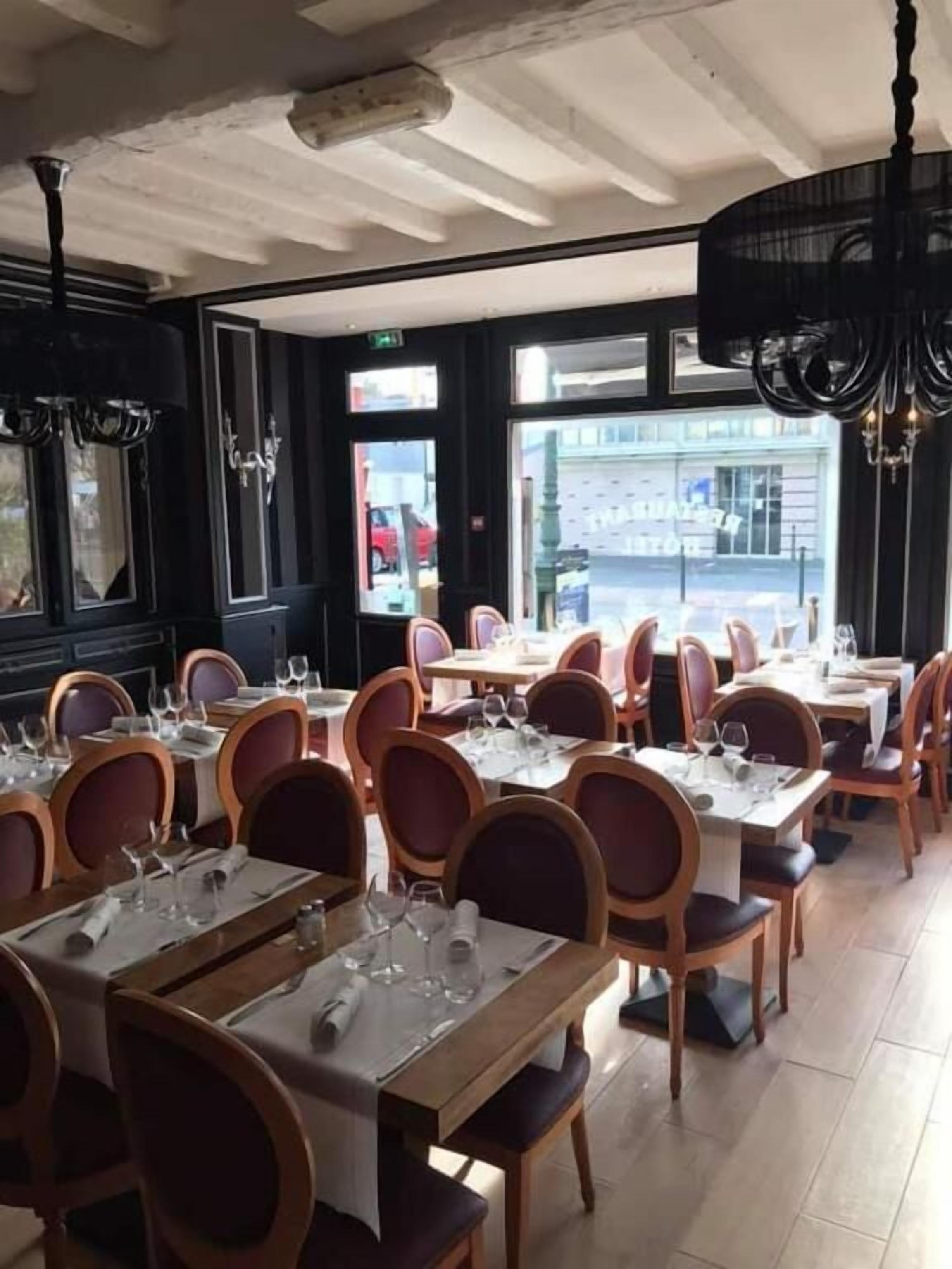 A restaurant with multiple tables set for dining, featuring wooden chairs and white tablecloths.