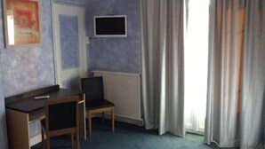 Une pièce comprenant un bureau, deux chaises, un téléviseur, un radiateur et une fenêtre avec des rideaux.