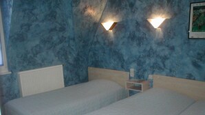 Une chambre avec deux lits simples, une table de chevet et un luminaire fixé au mur.