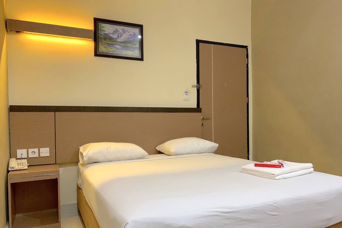 A hotel room with a bed, a nightstand, a telephone, and a framed picture on the wall.