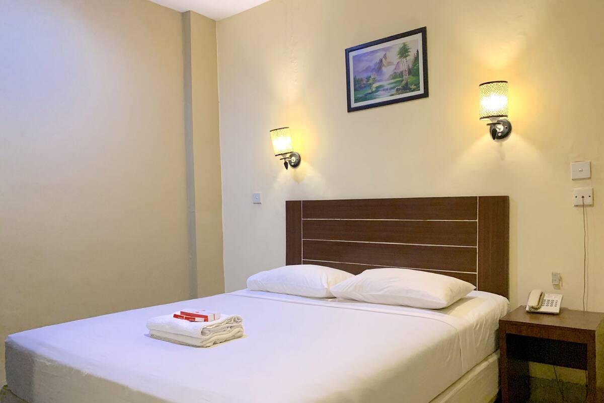 A hotel room with a neatly made bed, two wall-mounted lamps, a painting above the bed, and a bedside telephone.