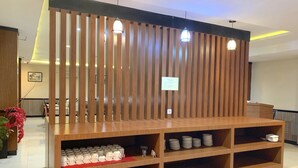 A reception desk with a wooden slat partition, a sign, and a shelf with mugs and plates.