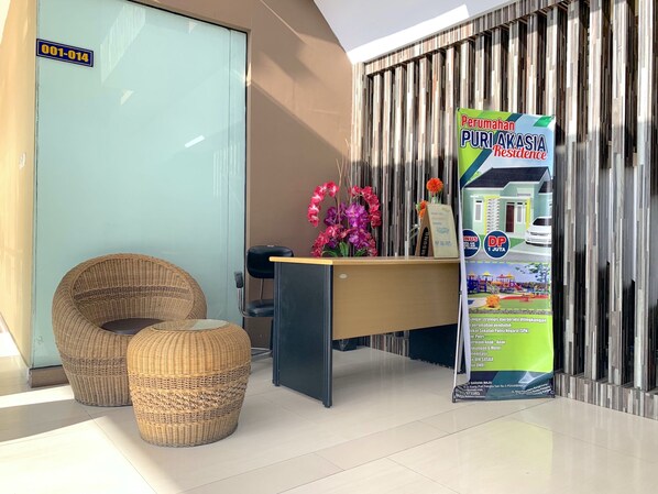 Un área de recepción con mostrador, sillas de mimbre, puerta de cristal y un cartel promocional.