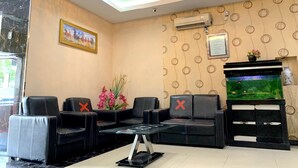 Un hall de hotel con sofás de cuero negro, una mesa de centro de vidrio, un equipo de aire acondicionado, un certificado enmarcado y un acuario.