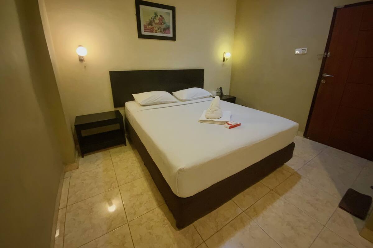 Habitación de hotel con una cama, dos mesitas de noche, una lámpara de noche, un cuadro en la pared y una puerta.