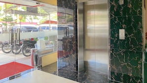 Un ascensor con pantalla digital, puerta de cristal y pared de mármol.