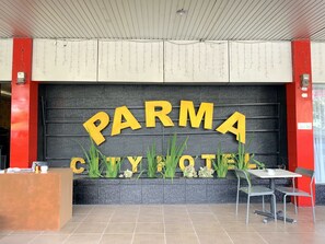 A reception desk, a sign with 'PARMA CITYHOTEL' in large yellow letters, and a seating area with a table and chairs.
