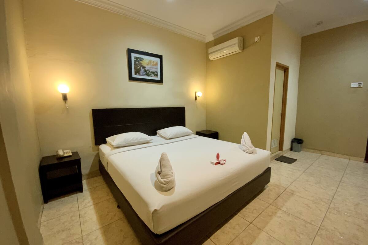 Una habitación de hotel con una cama grande, dos mesitas de noche, un equipo de aire acondicionado y un cuadro enmarcado en la pared.