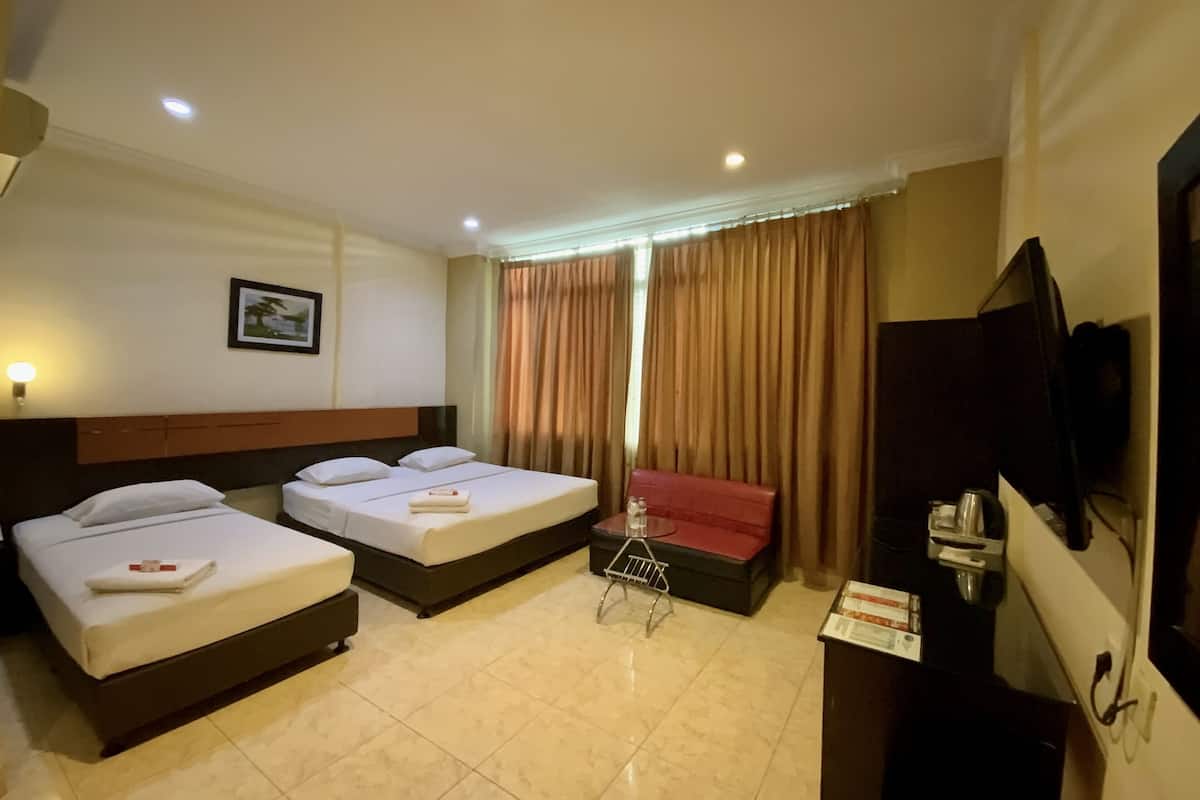 Habitación de hotel con dos camas, un sofá rojo, un televisor y una mesita con hervidor y tazas.