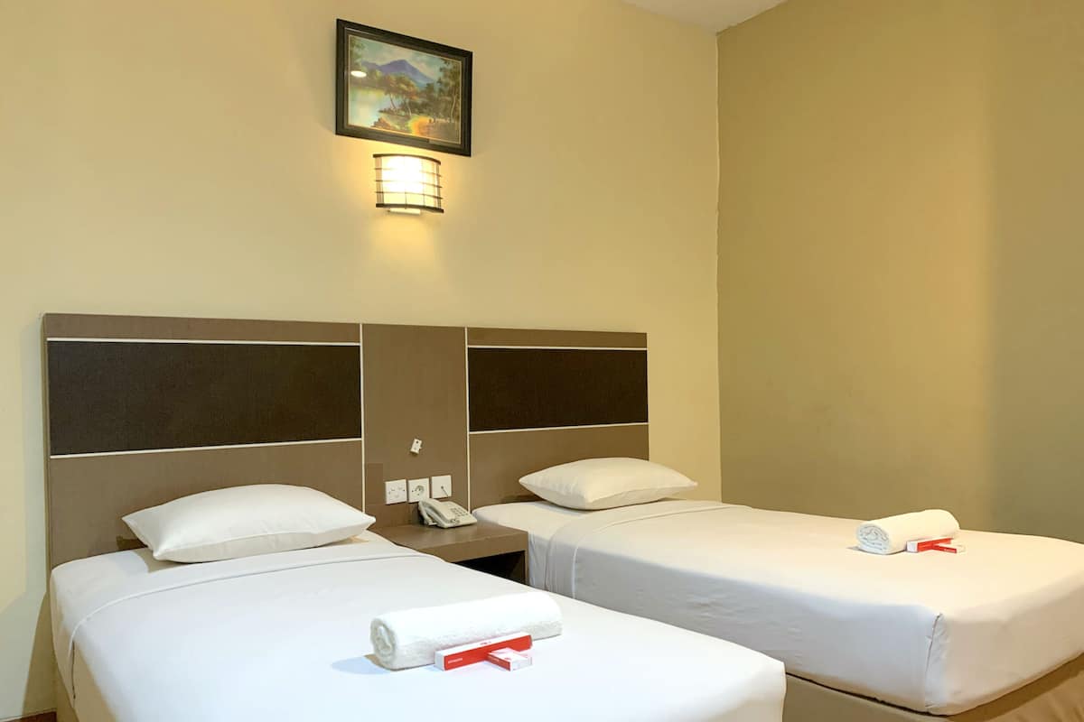 A hotel room with two beds, a nightstand, a phone, and a painting on the wall.