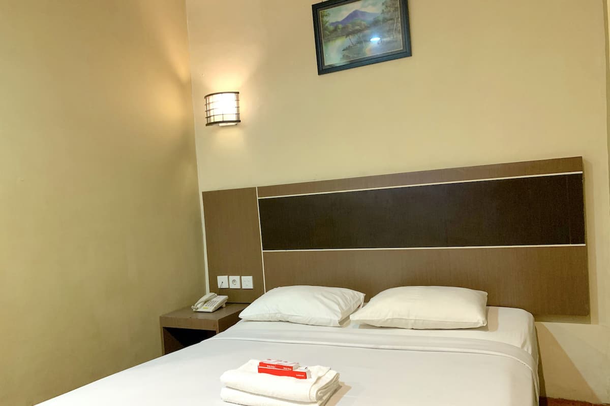 A hotel room with a large bed, a nightstand with a phone, and a wall-mounted light.