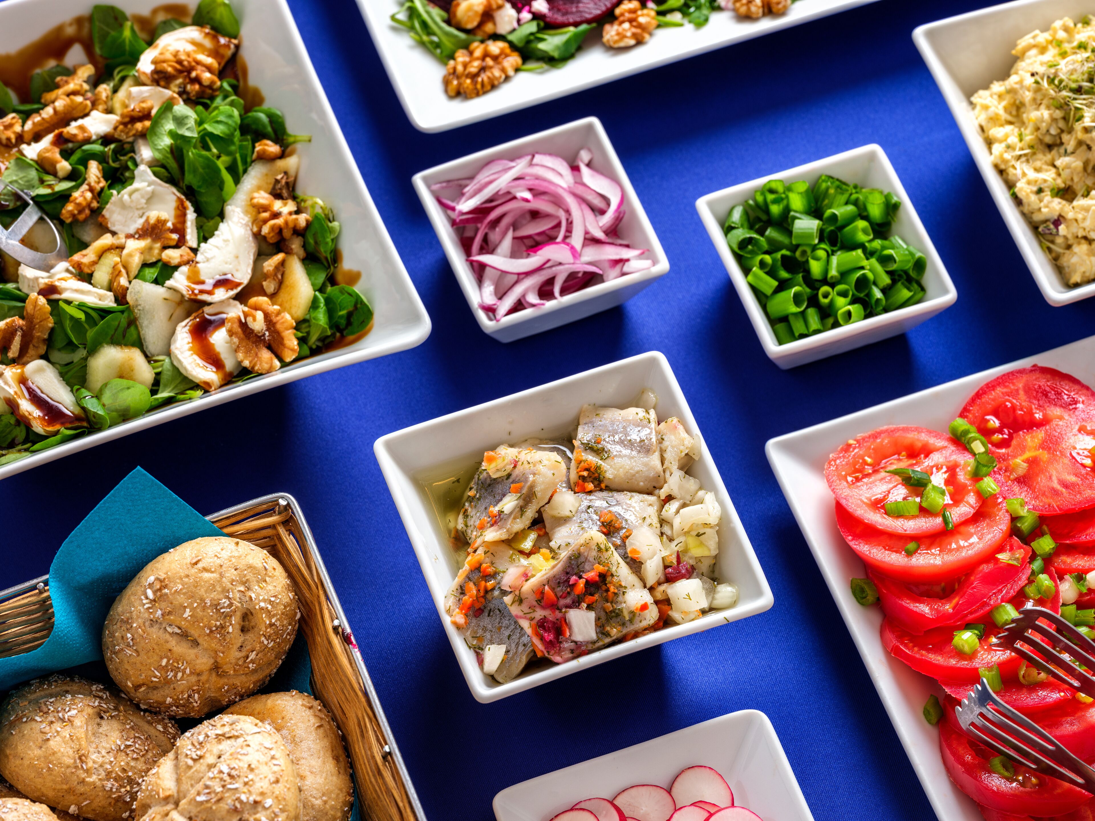 A variety of dishes including a salad with walnuts, a bowl of sliced radishes, and a dish with fish and vegetables.