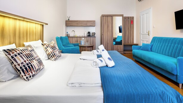 A hotel room with a bed, a blue sofa, a small table, and a kitchenette in the background. - Kosmopolita Apartments (Kraków)