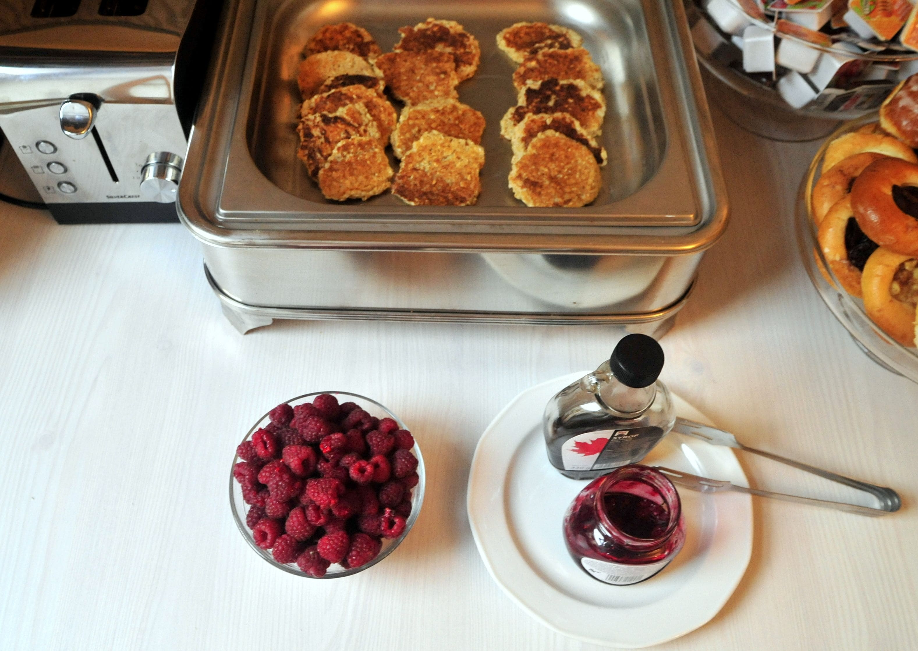 A buffet table with a variety of food items including a bowl of raspberries, a plate with a jam container, and a tray with breaded items.