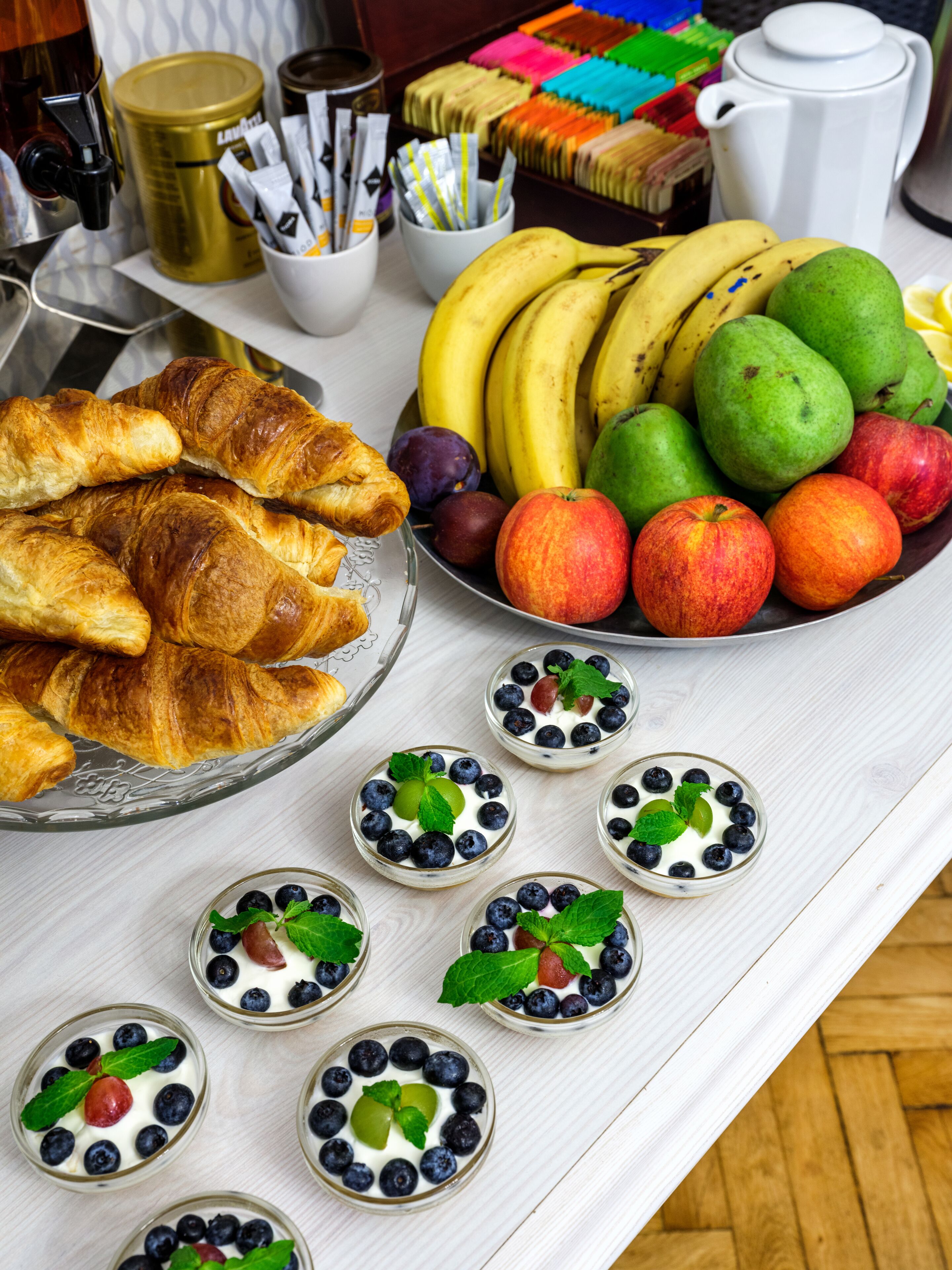 A breakfast buffet with croissants, fruits, and yogurt parfaits.