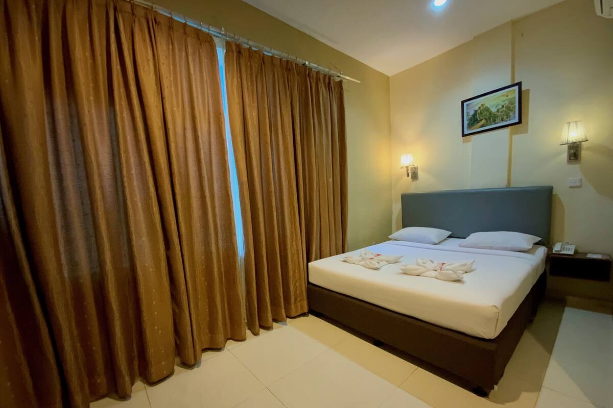 A hotel room with a large bed, a nightstand, a lamp, and a painting on the wall.
