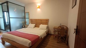 A bedroom with a wooden bed, a small table with a chair, and a wall-mounted light. - Easy Homes (Lalitpur)