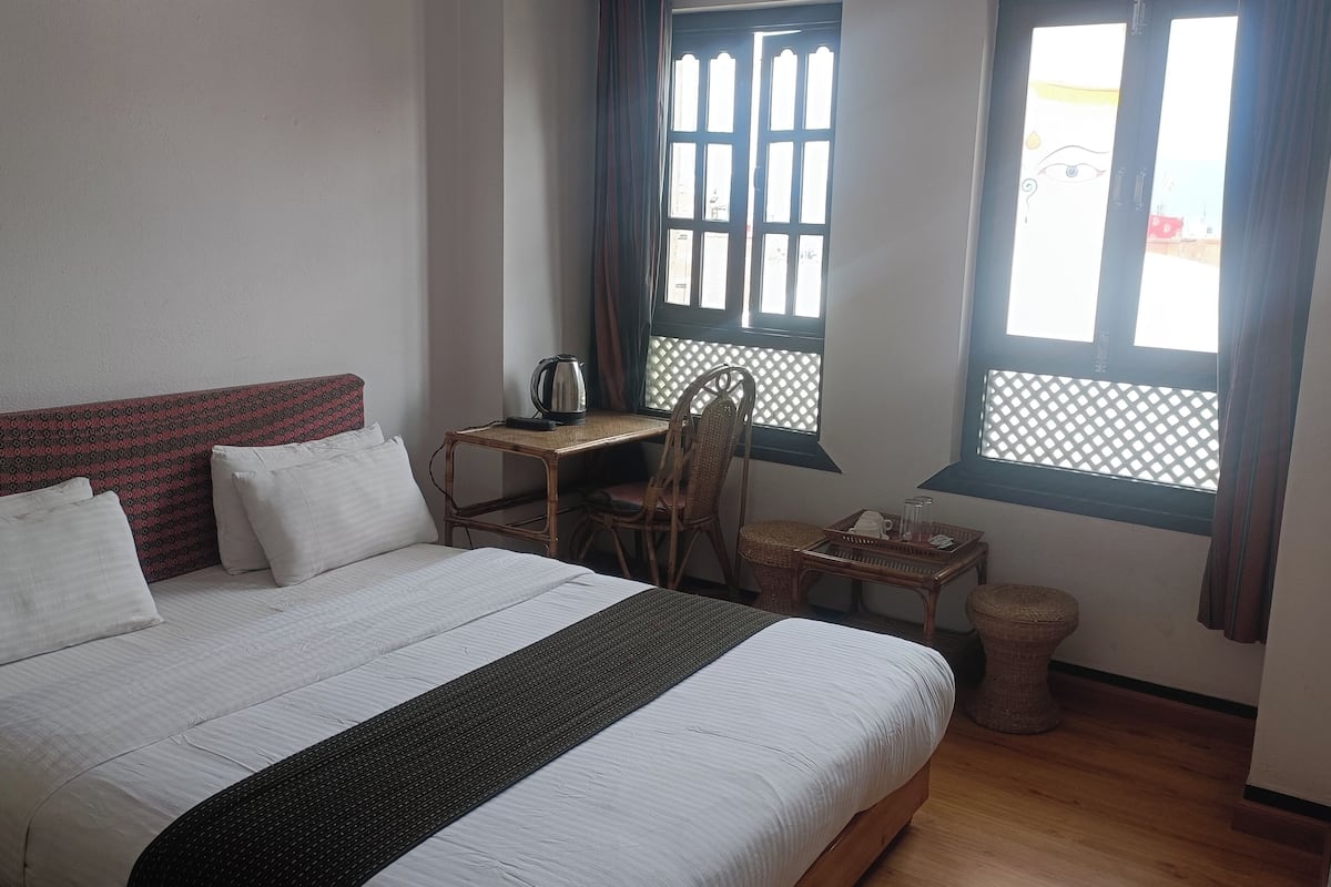 Un dormitorio con cama, escritorio, silla, mesita y ventana con diseño de celosía.