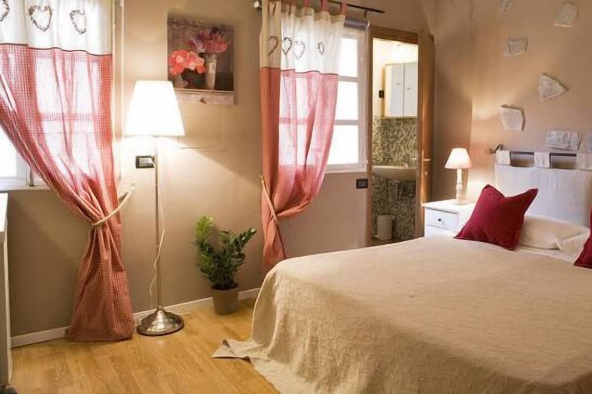 A bedroom with a large bed, two bedside tables, a nightstand, a lamp, a mirror, and a potted plant.