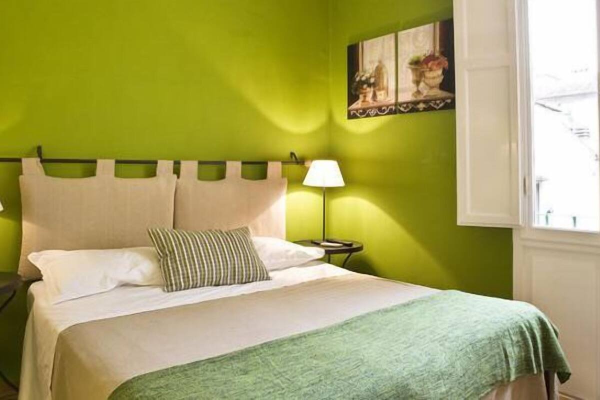 A bed with a green blanket, two bedside lamps, and a nightstand.
