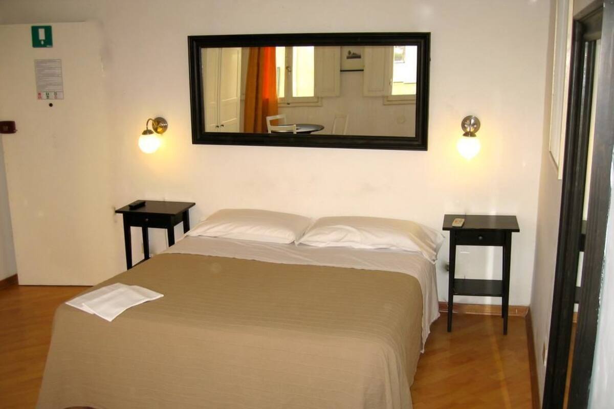 A hotel room with a large bed, two bedside tables, a mirror above the bed, and a door to the right.