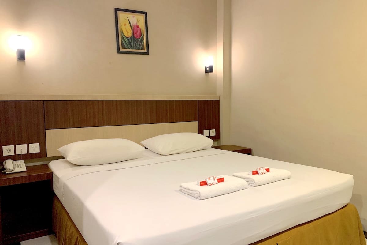 A hotel room with a bed, two bedside tables, a wall-mounted telephone, and a painting.