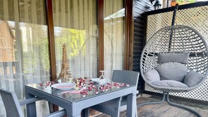Een eethoek met een tafel voor twee personen, een rieten stoel en een hangstoel met kussens.