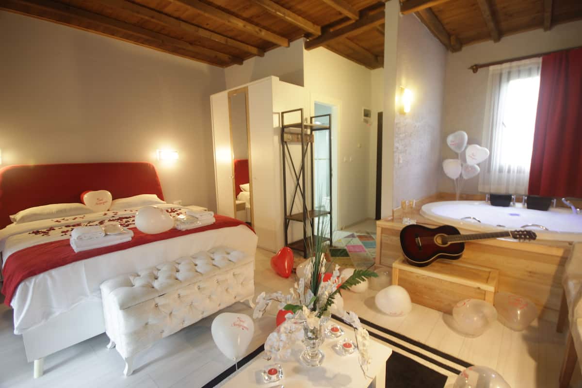 Quarto de hotel com uma cama grande, área de estar, banheiro com banheira e um violão.