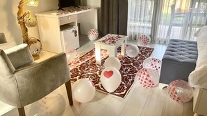 Een moderne woonkamer met een flatscreen televisie, een wit bureau en een bank. Er liggen hartjesballonnen verspreid.