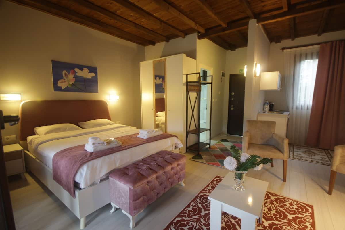 Quarto com cama, mesa de cabeceira, banquinho e uma pequena mesa com um vaso.