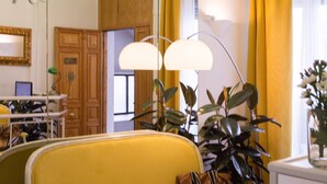 Un sofá amarillo en una habitación con puerta de madera, una araña verde y cortinas amarillas.