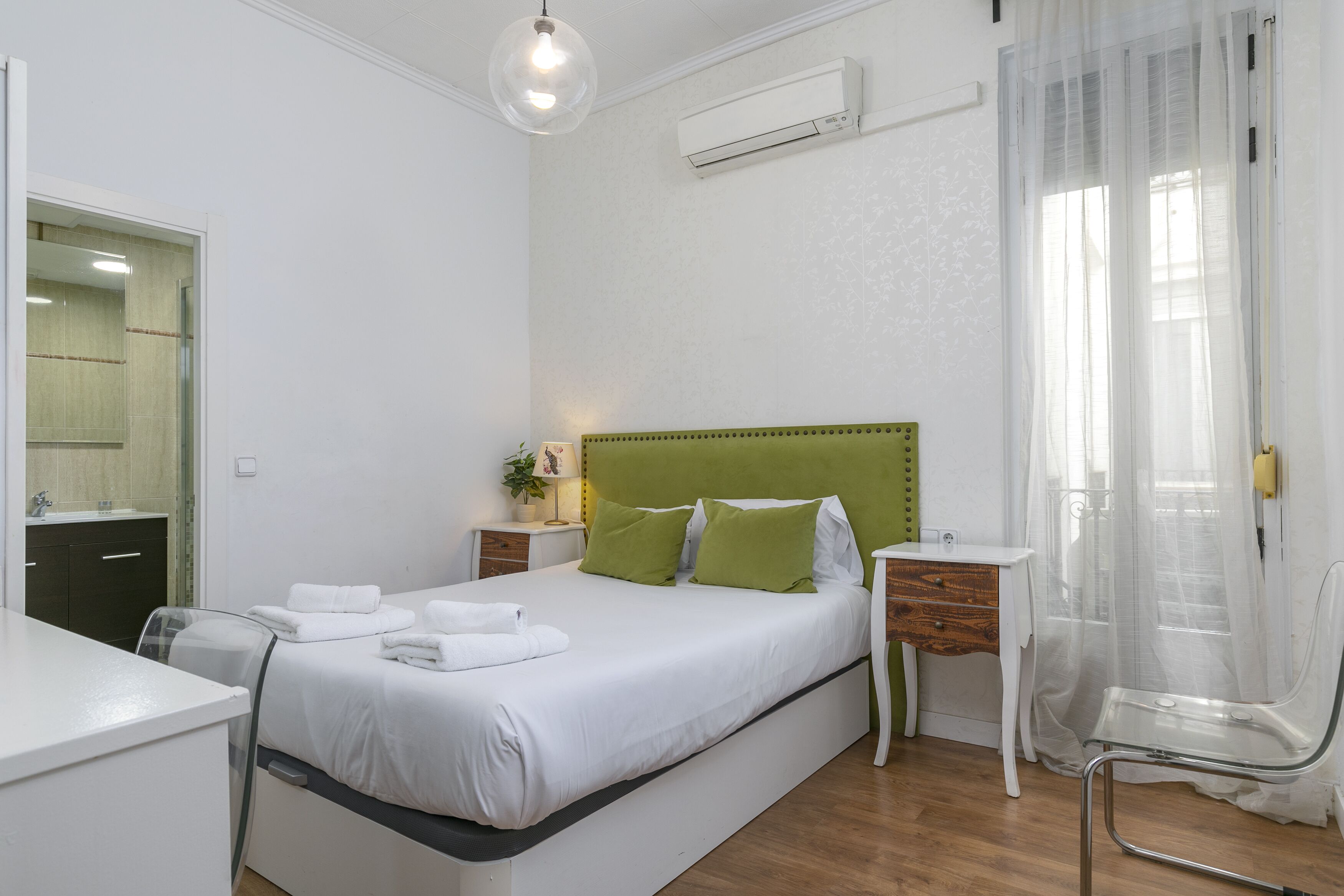 A bedroom with a bed, bedside table, chair, and an air conditioning unit.