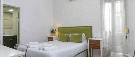 A bedroom with a bed, bedside table, chair, and an air conditioning unit.