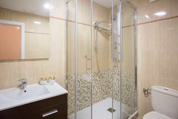 A bathroom with a glass-enclosed shower, a sink with a mirror, and a toilet.