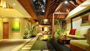 A modern indoor courtyard with a wooden ceiling, a seating area with a sofa and coffee table, and a pathway leading to a pool. - The Hotman Paris II Seminyak (Seminyak)