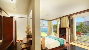 A bedroom with a bed, a TV, a desk, and a chair. There is a window with curtains and a view of the ocean. - The Cliff Hotman Paris VI Pandawa (Kutuh)
