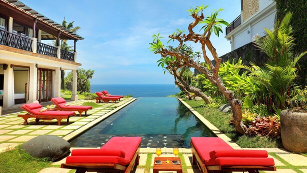A poolside area with red lounge chairs, a clear view of the ocean, and lush greenery. - The Cliff Hotman Paris VI Pandawa (Kutuh)