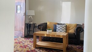 Een woonkamer met een kamerbreed tapijt, een houten salontafel, een leren bank en een bijzettafeltje met een lamp.