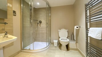 Un baño moderno con ducha envuelta en vidrio, inodoro blanco y lavamanos con espejo.