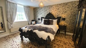 Een slaapkamer met een groot bed, een versierd hoofdeinde, bloemenbehang en een kroonluchter.