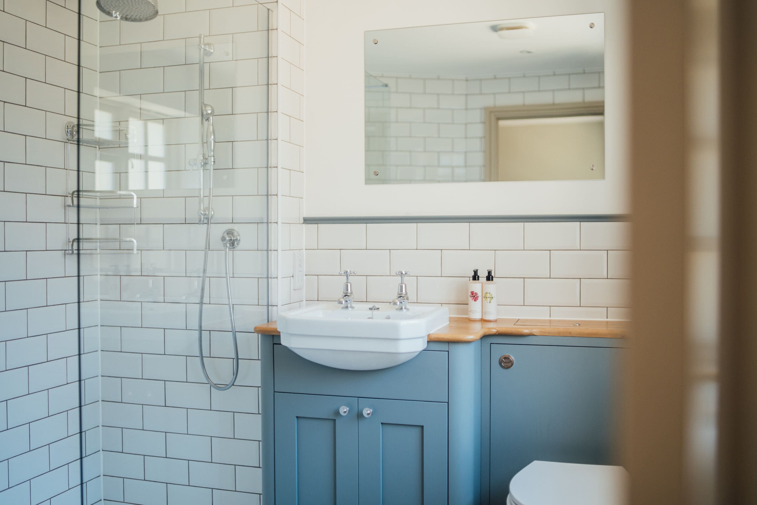 Un bany amb dutxa de vidre, un lavabo amb taulell de fusta i un mirall sobre el lavabo.