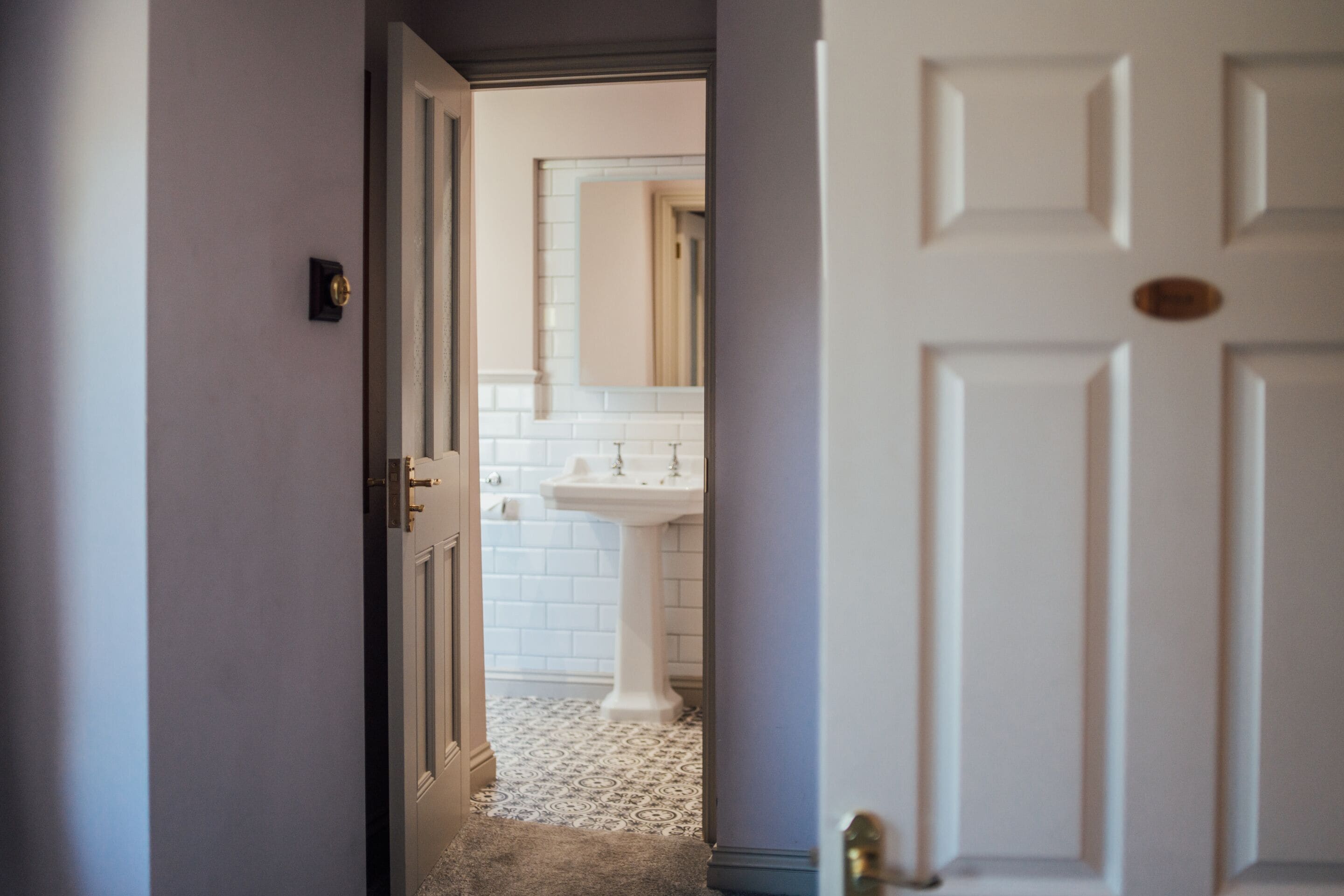 Un pasillo que conduce a un baño con un lavamanos blanco y suelo de baldosas.