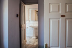 A hallway leading to a bathroom with a white sink and tiled floor. - Farthings Hotel and Restaurant (Taunton)