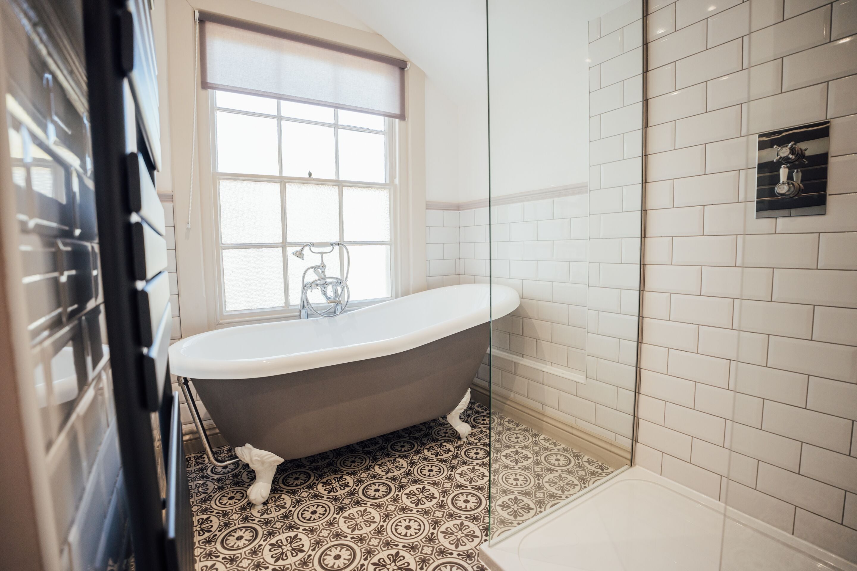 A bathroom with a freestanding bathtub, a window, patterned floor tiles, and a shower area.